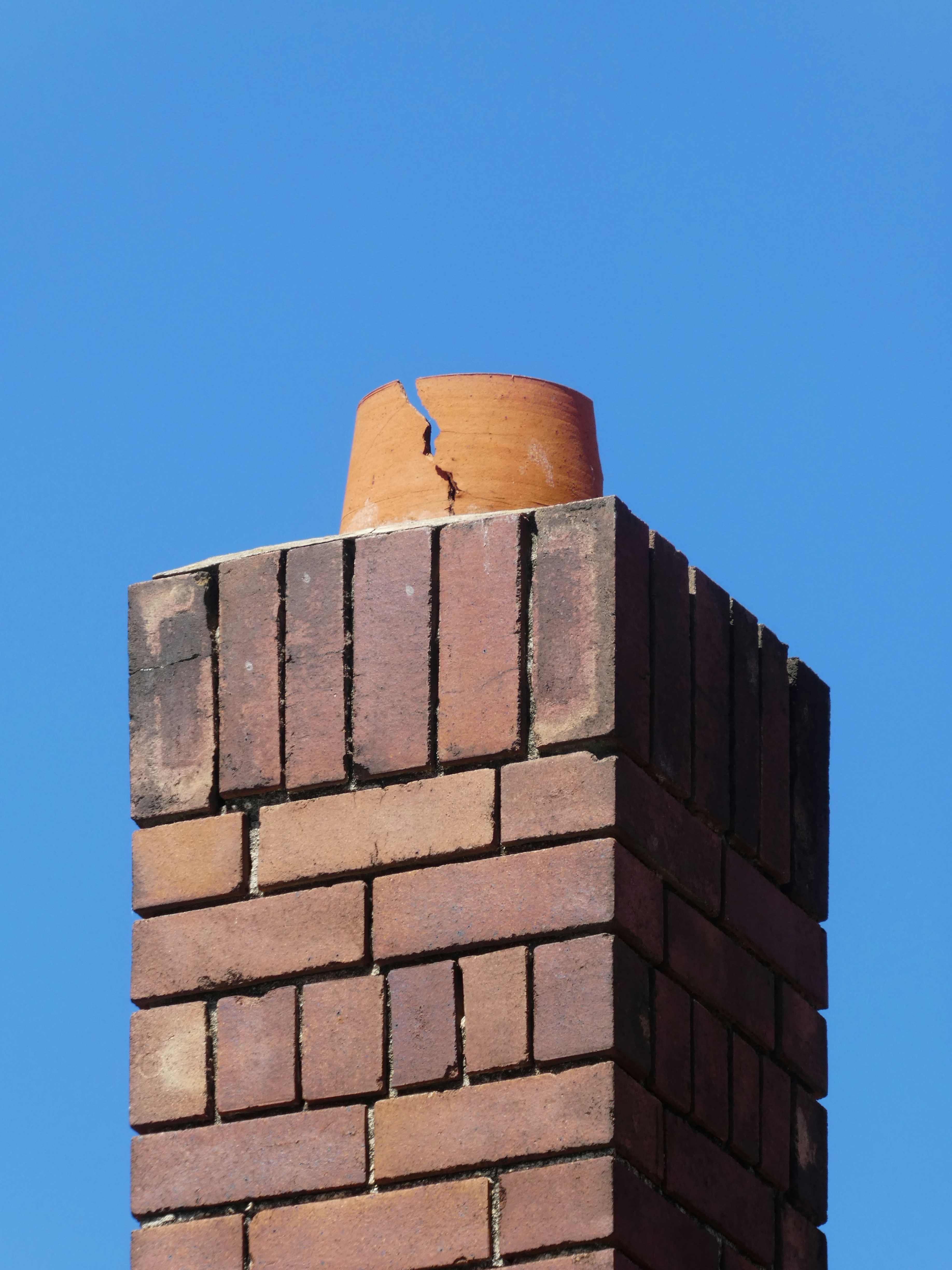 Damaged chimney flue tile and weathered masonry viewed against the sky